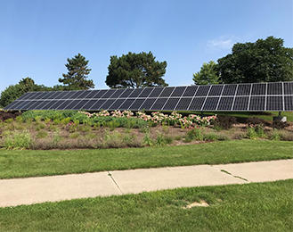 Large solar panel outside the Municipal Building behind a patch of flowers. 