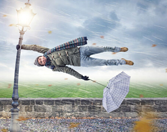 Stock photo of someone holding onto a lamp post with an umbrella because the wind is blowing them away.