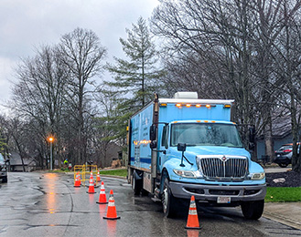 Large blue construction truck parked on the road with orange cones blocking it off.